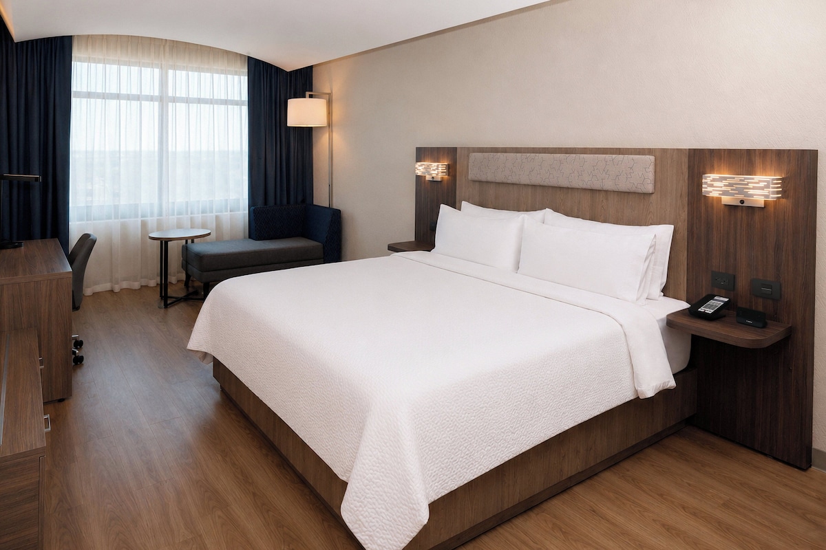 Una camera d'albergo con un letto grande, una scrivania, una sedia, un tavolino e una lampada.