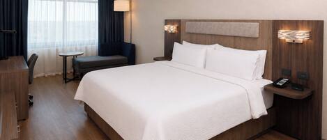 Una habitación de hotel con una cama grande, un escritorio, una silla, una mesita y una lámpara.