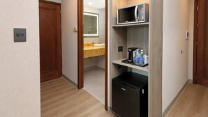 Quarto de hotel com piso de madeira, micro-ondas embutido, geladeira, pia e espelho.