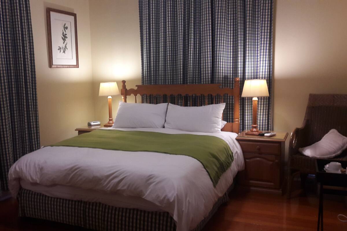 A hotel room with a large bed, two bedside lamps, a wooden headboard, a chair, and a framed picture on the wall.