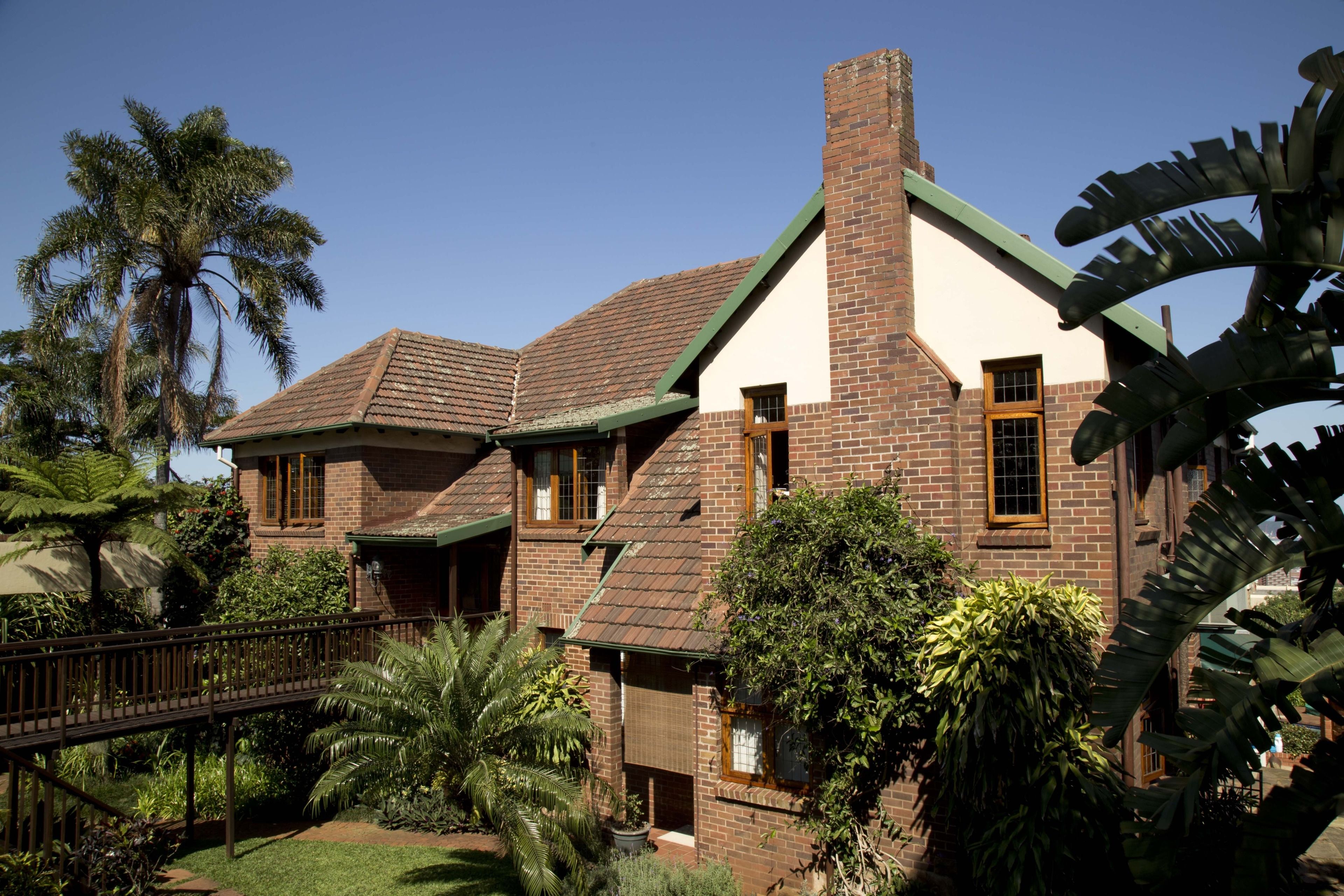 A two-story house with a brick exterior, green roof, and a brick chimney.