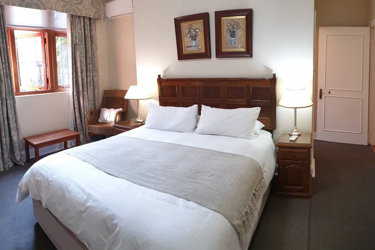 A hotel room with a large bed, two bedside tables with lamps, a wooden headboard, a small bench, and a door with a number.