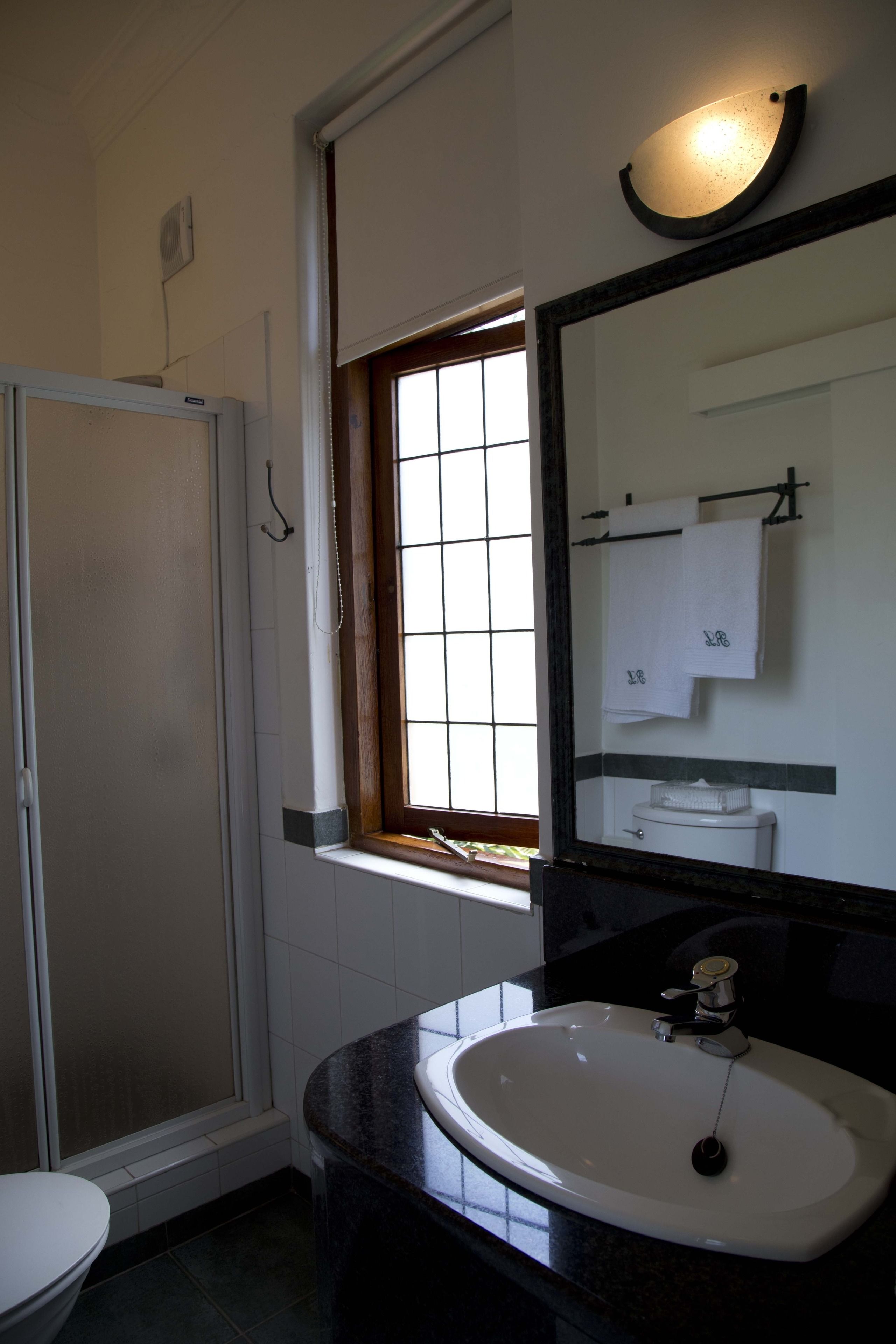 Een badkamer met een wit toilet, een zwarte wastafel met een spiegel erboven en een raam met uitzicht.
