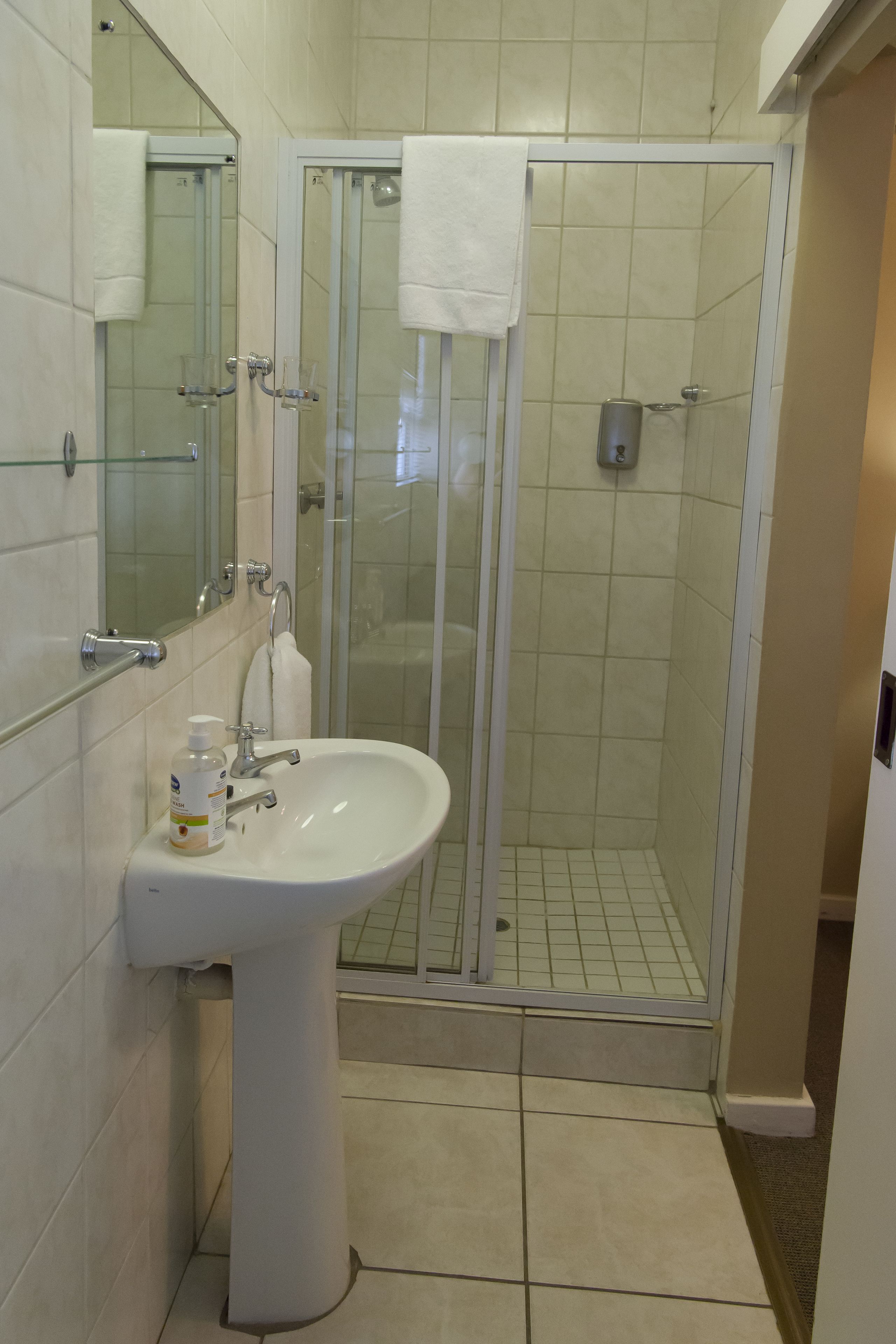 A bathroom with a glass-enclosed shower, a sink with a bottle of hand soap, and a mirror.
