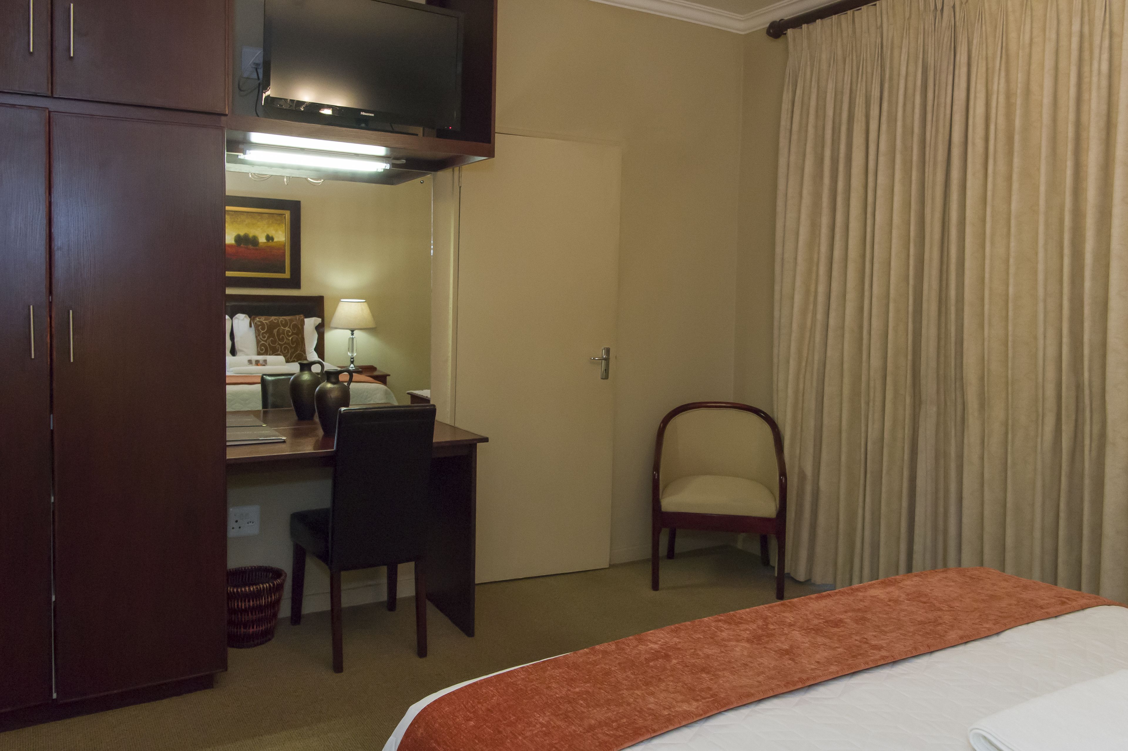 Ein Hotelzimmer mit Bett, Schreibtisch mit Stuhl, Fernseher und einem Fenster mit Vorhängen.