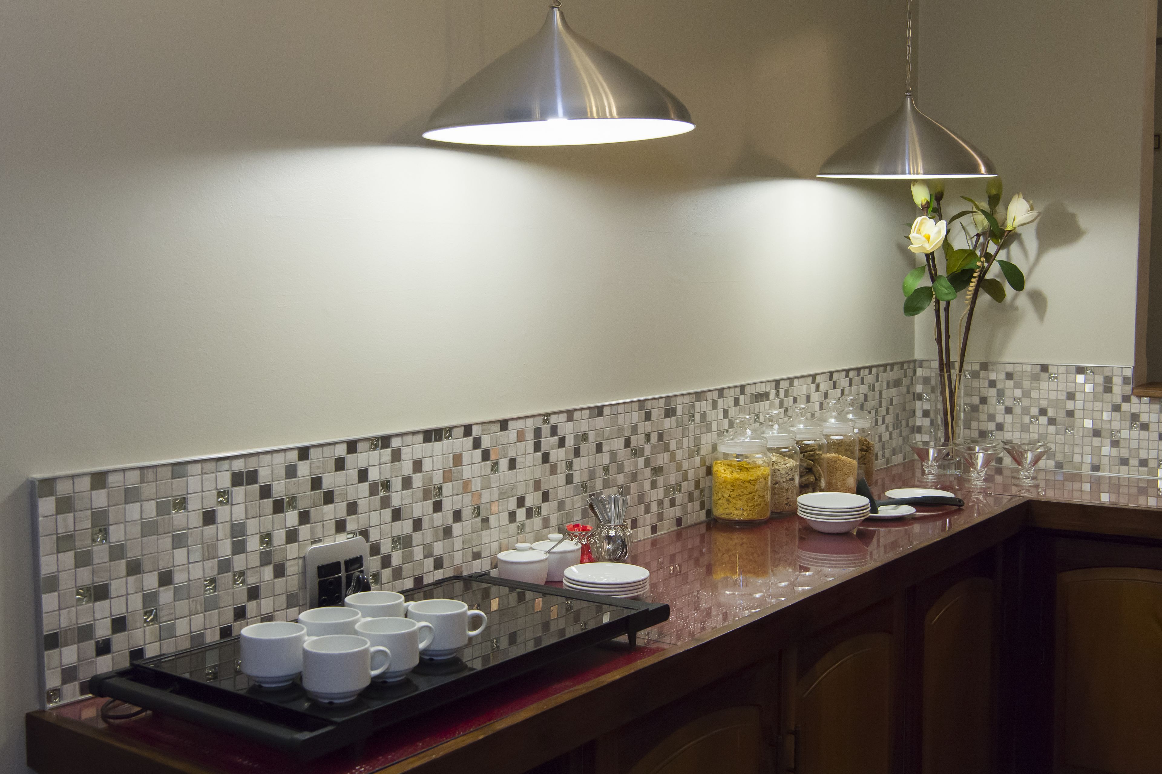 A kitchen counter with a tray of white cups, a coffee maker, and a jar of sugar.