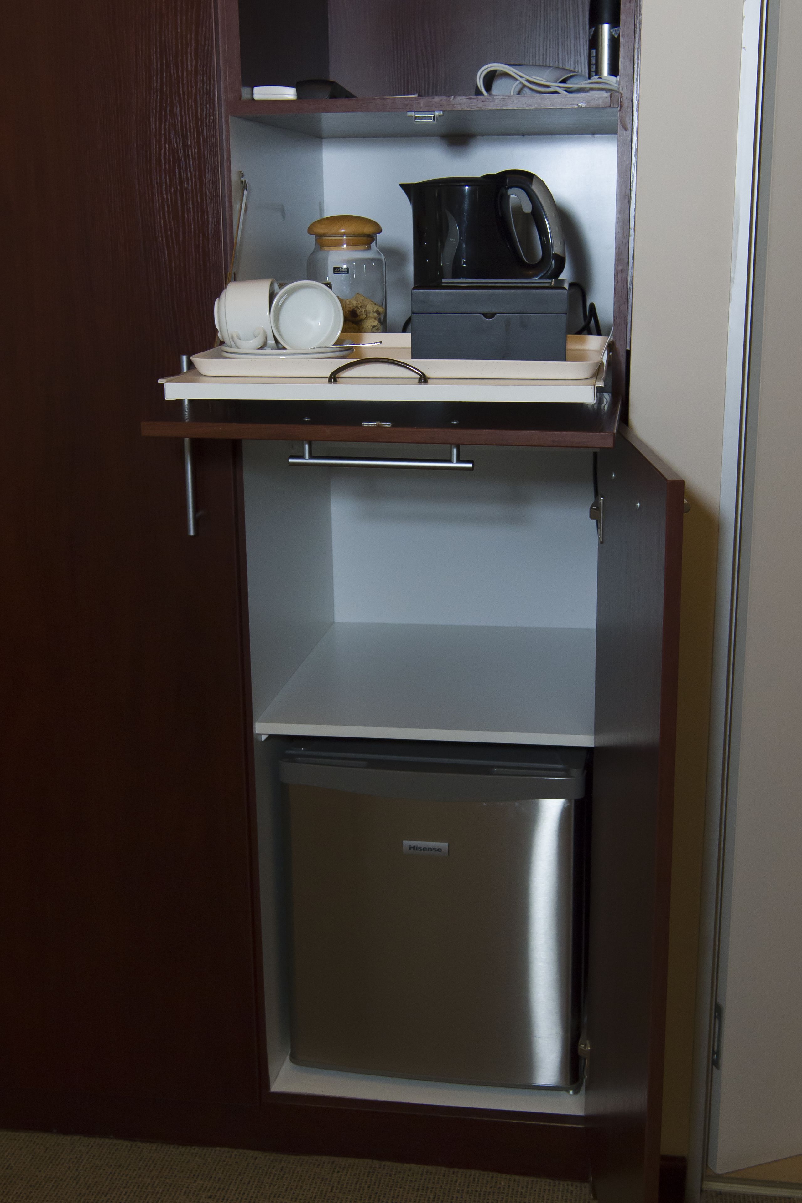 A compact kitchenette with a stainless steel refrigerator, a coffee maker, and a jar.