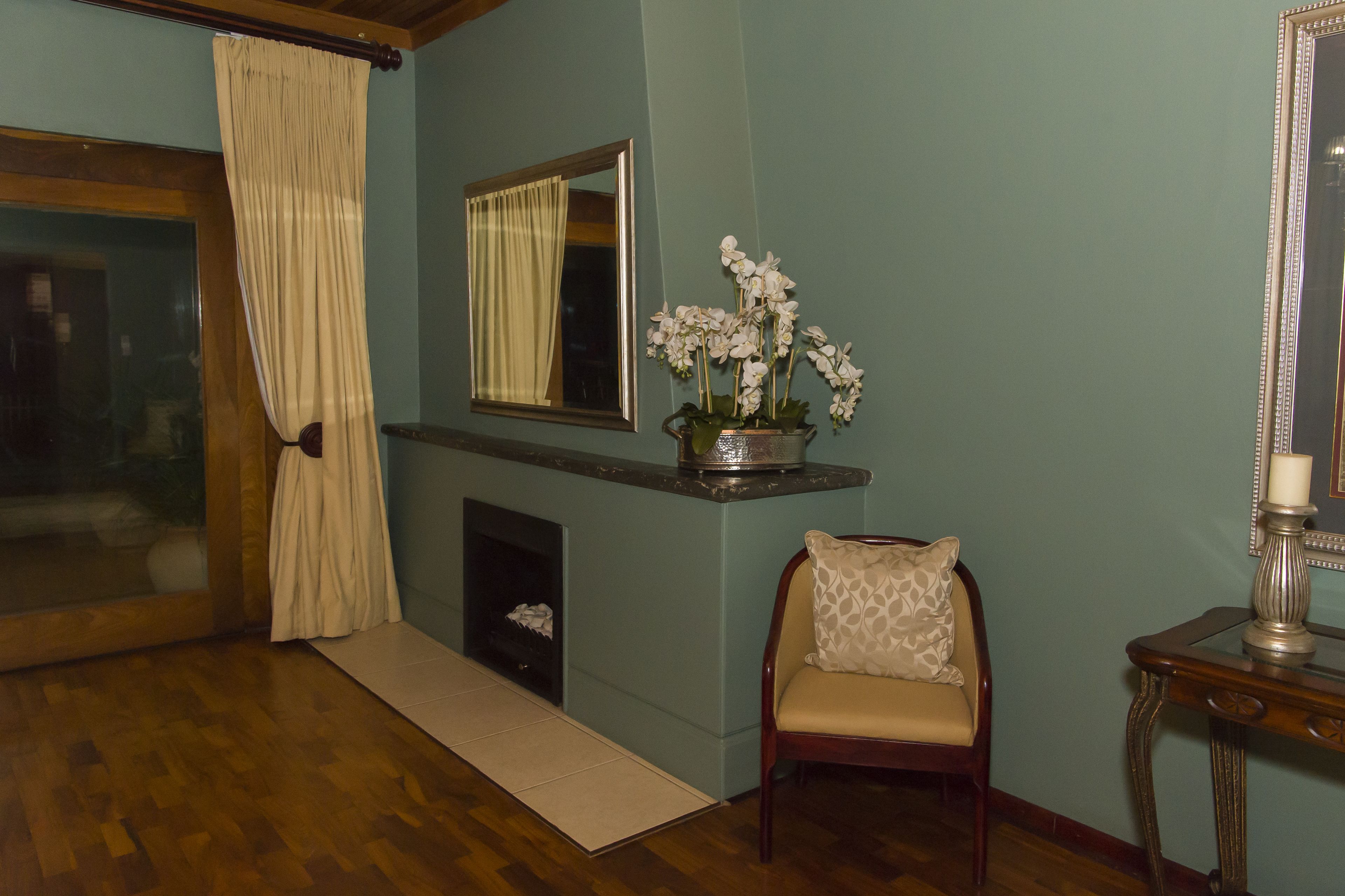 A room with a wooden floor, a chair with a patterned cushion, a vase with white flowers, a mirror, and a fireplace.