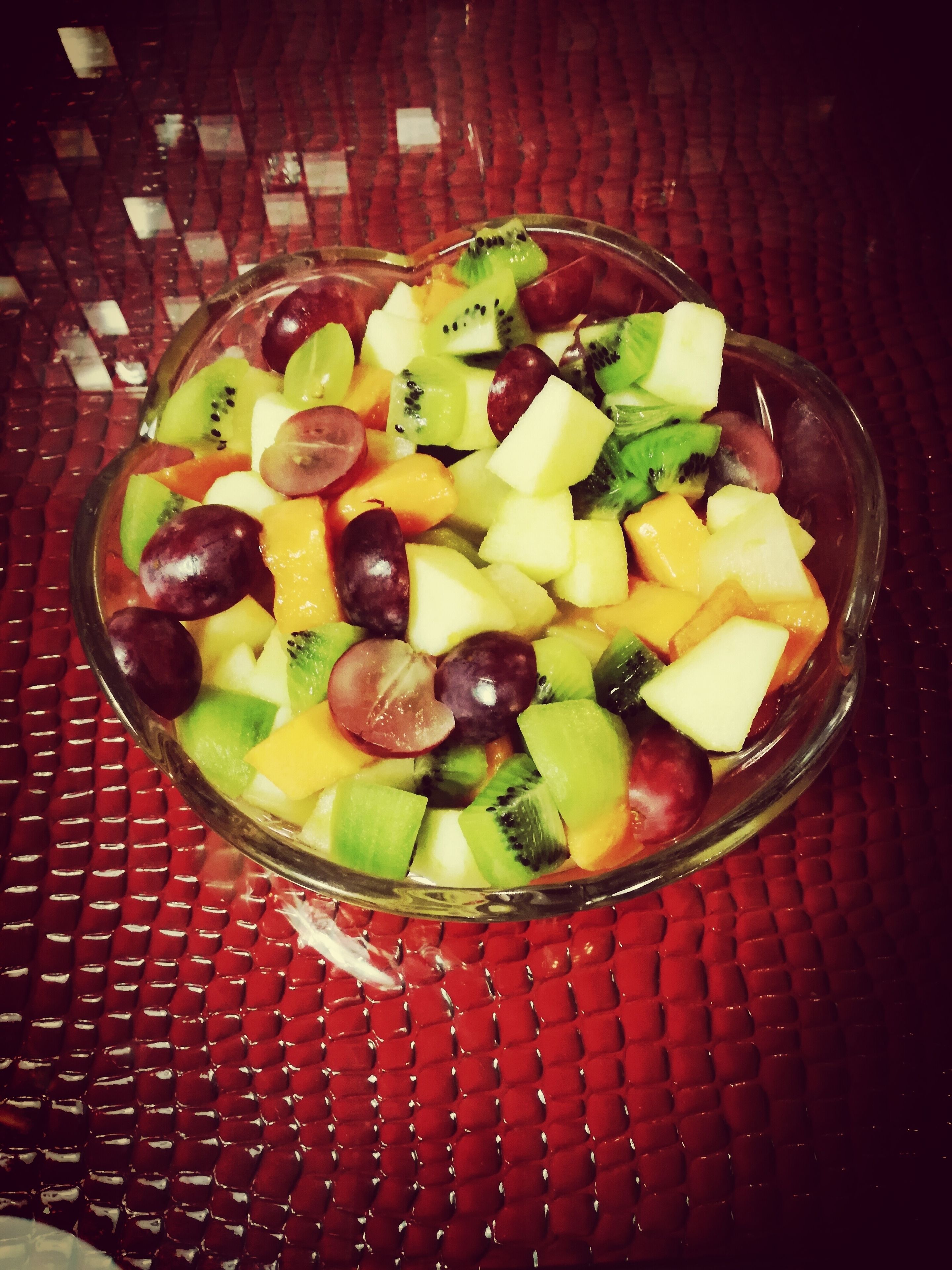Un tazón de ensalada de frutas sobre una mesa roja con textura.