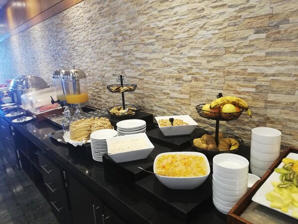 A buffet with various food items and beverages, including fruits, cereals, and a juice dispenser.