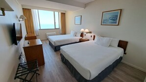 Ett hotellrum med två sängar, ett skrivbord, en stol, en TV och ett fönster med gardiner.