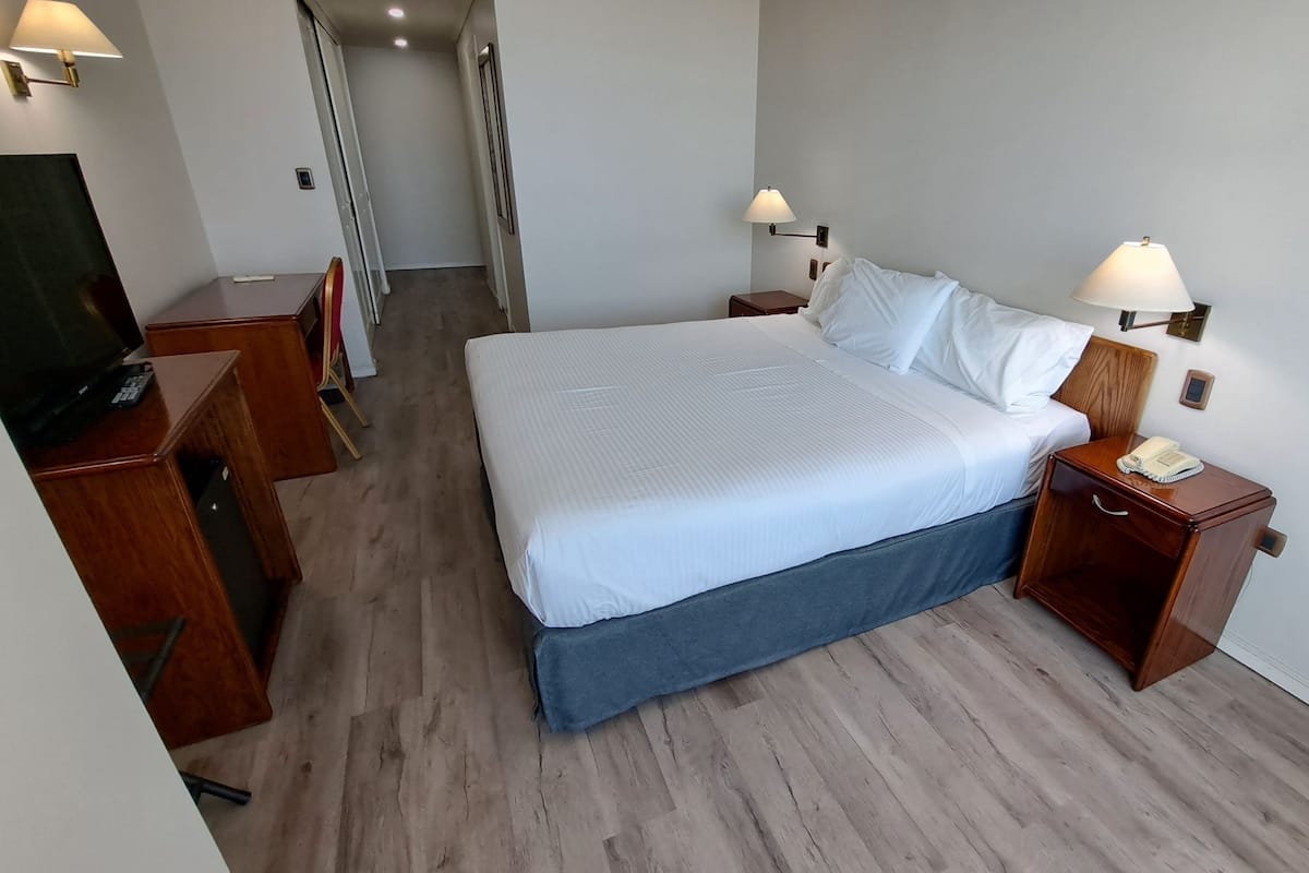 Et hotelværelse med en seng, sengeborde med lamper og telefon, samt et fjernsyn på et stativ og en stol.