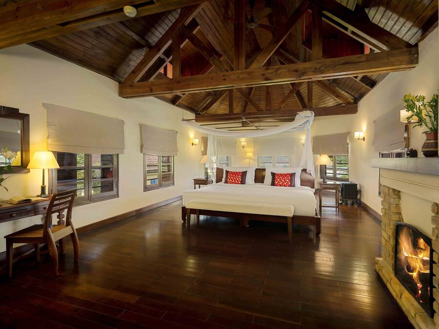 A spacious bedroom with a large bed, wooden beams, a fireplace, and a desk with a chair.