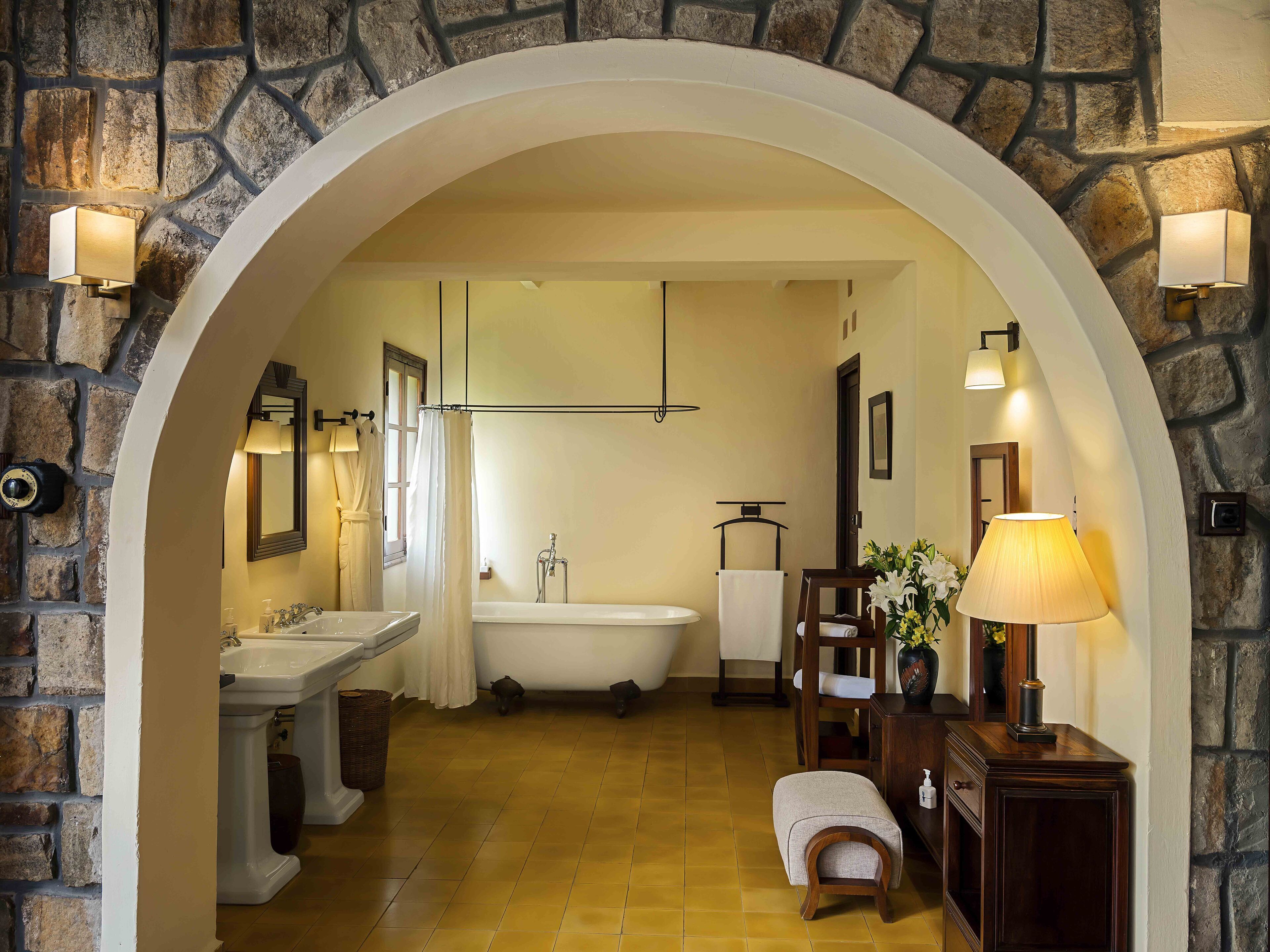 A bathroom with a stone wall, a bathtub, a sink, a mirror, and a towel rack.