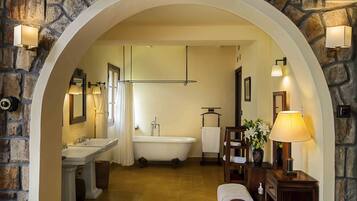 Un baño con pared de piedra, una bañera, un lavabo, un espejo y un perchero para toallas.