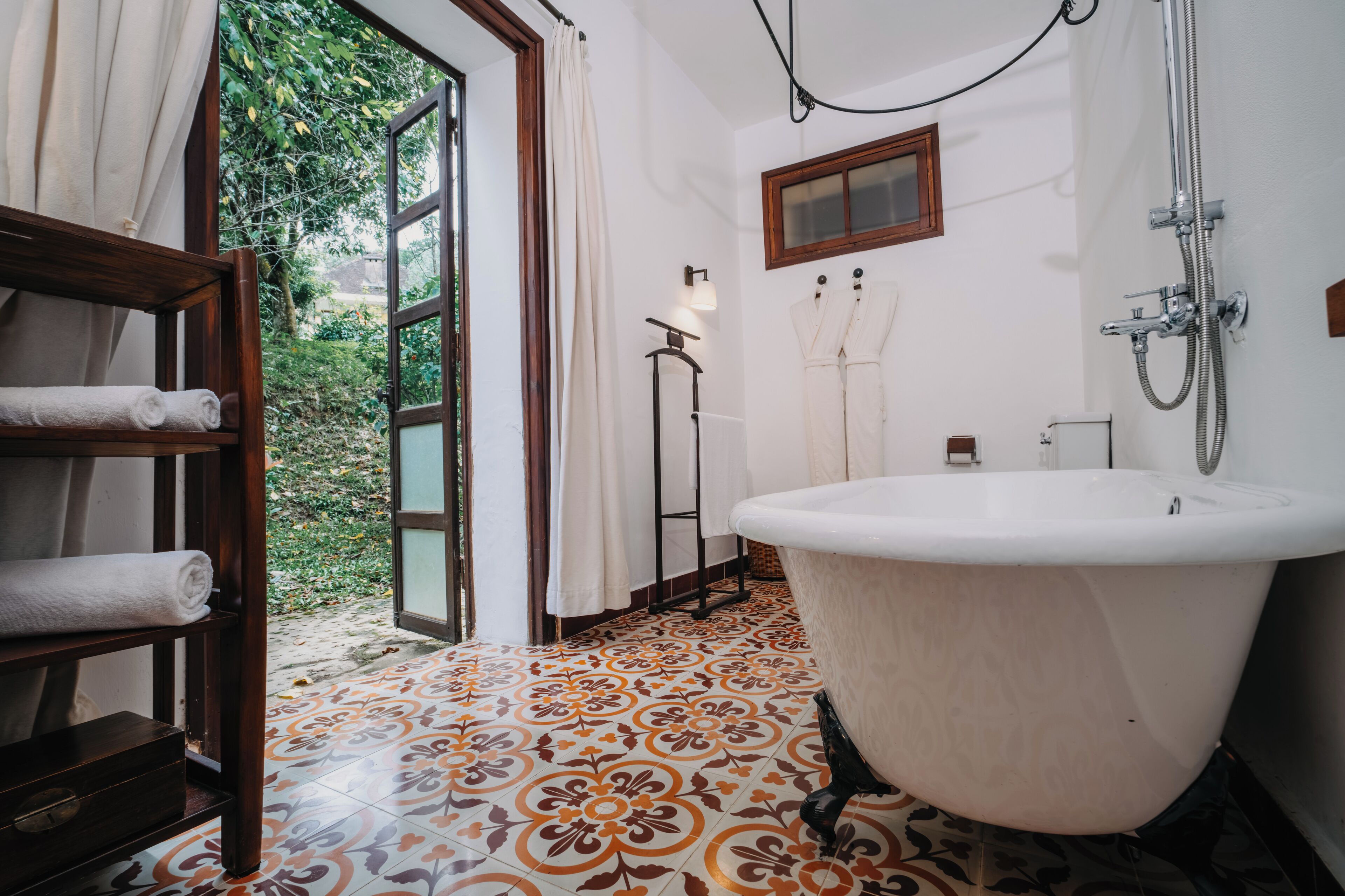 Une salle de bain avec une baignoire sur pieds, une étagère en bois avec des serviettes et une fenêtre avec des rideaux.