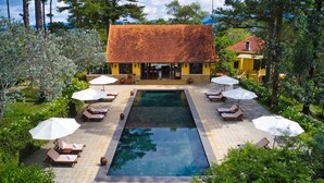 A pool area with lounge chairs and umbrellas, surrounded by greenery and a building with a tiled roof. - Ana Mandara Villas Dalat Resort & Spa (Cam Ly - Da Lat)