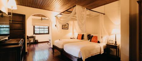 A bedroom with a canopy bed, wooden flooring, and a desk with a lamp.