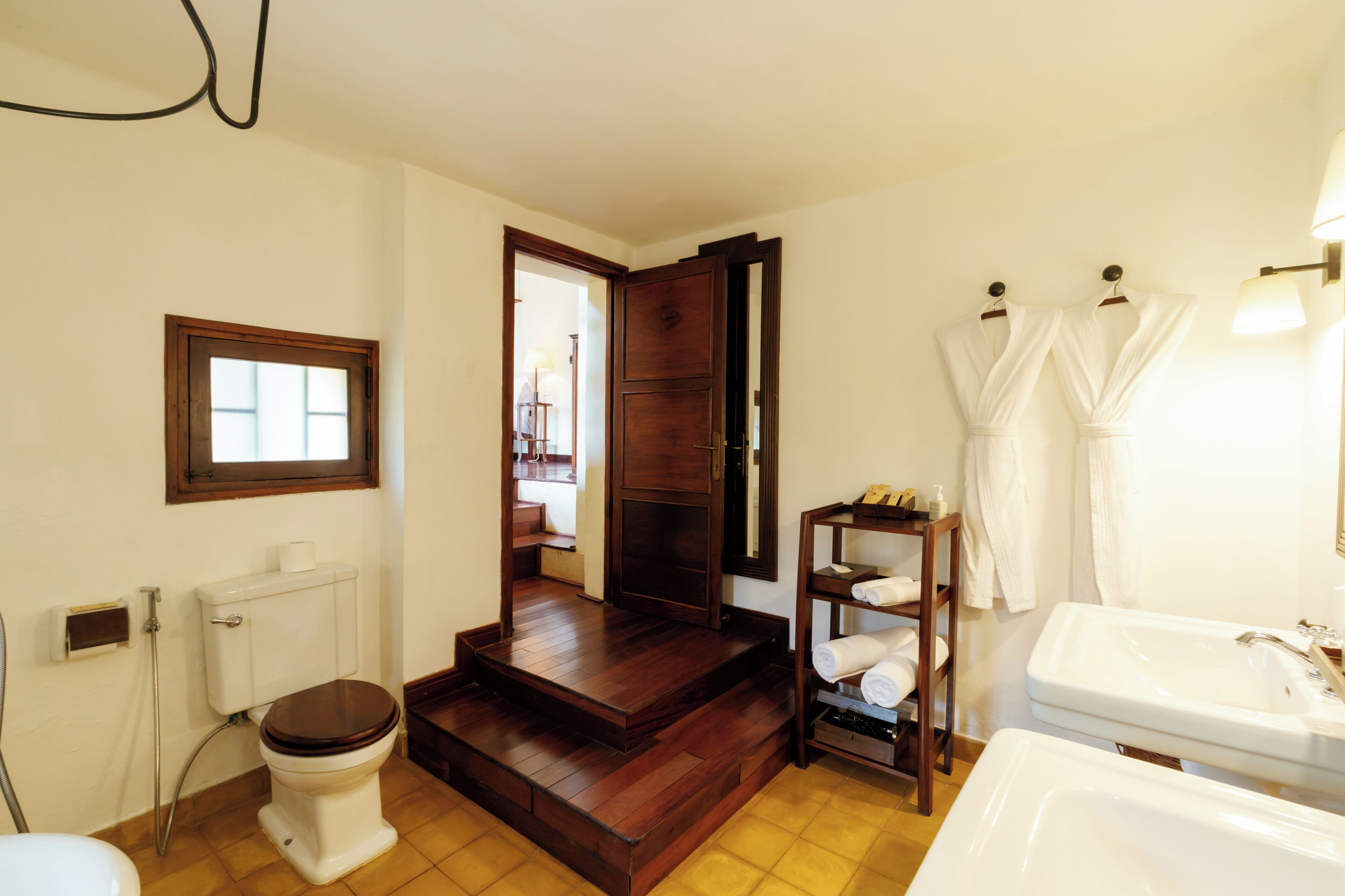 A bathroom with a toilet, a sink, a shower, and a wooden staircase leading to a door.