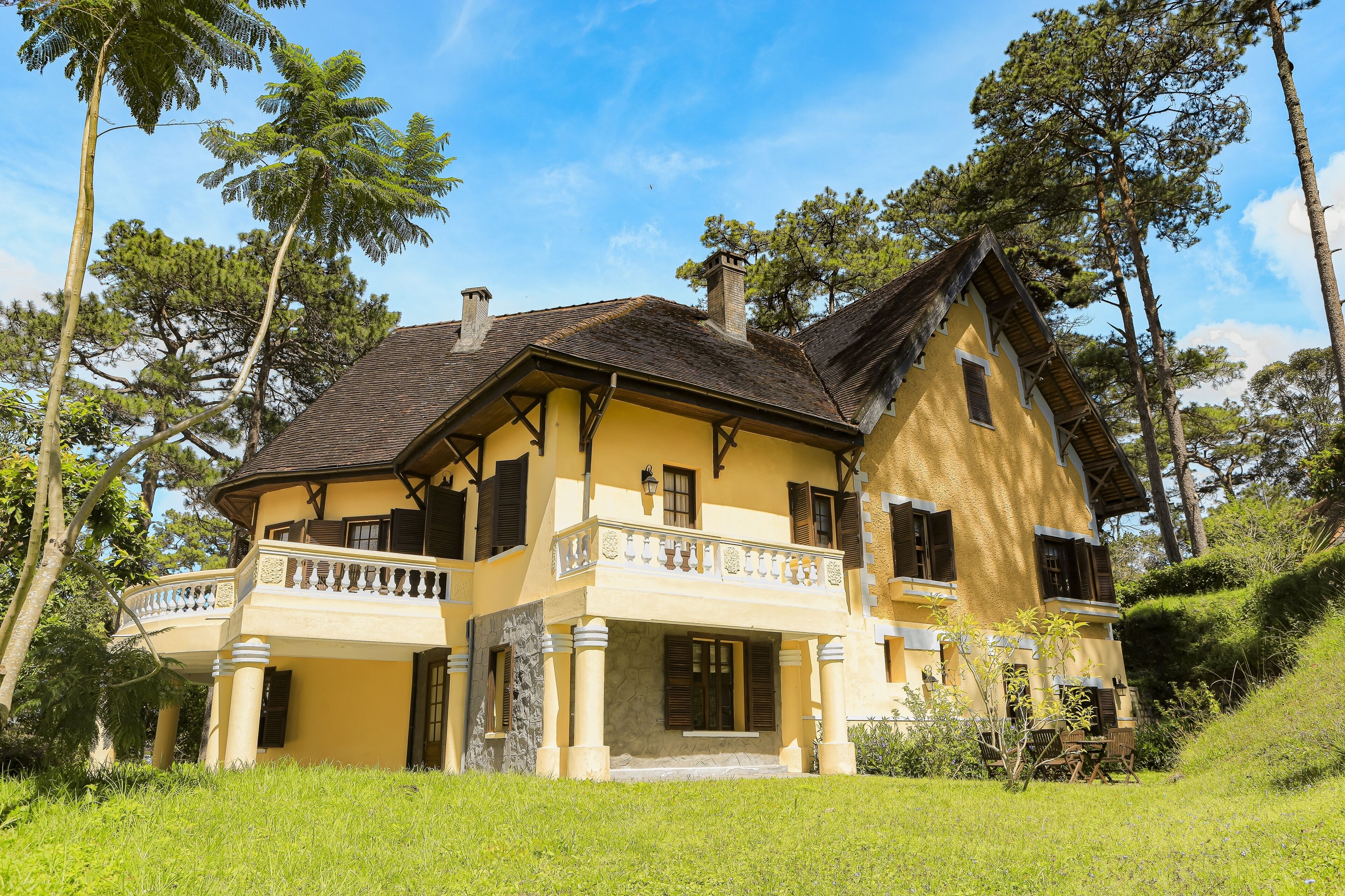Une maison à deux étages avec un balcon, entourée d’arbres et d’herbe.