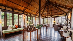A spacious room with a high wooden ceiling, large windows, a wooden bench, a table with candles, and a sofa. - Ana Mandara Villas Dalat Resort & Spa (Cam Ly - Da Lat)