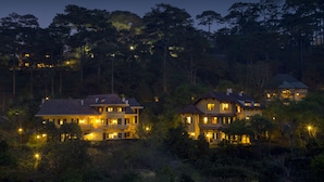 A large, multi-story house with multiple windows and balconies, surrounded by dense trees and other houses. - Ana Mandara Villas Dalat Resort & Spa (Cam Ly - Da Lat)