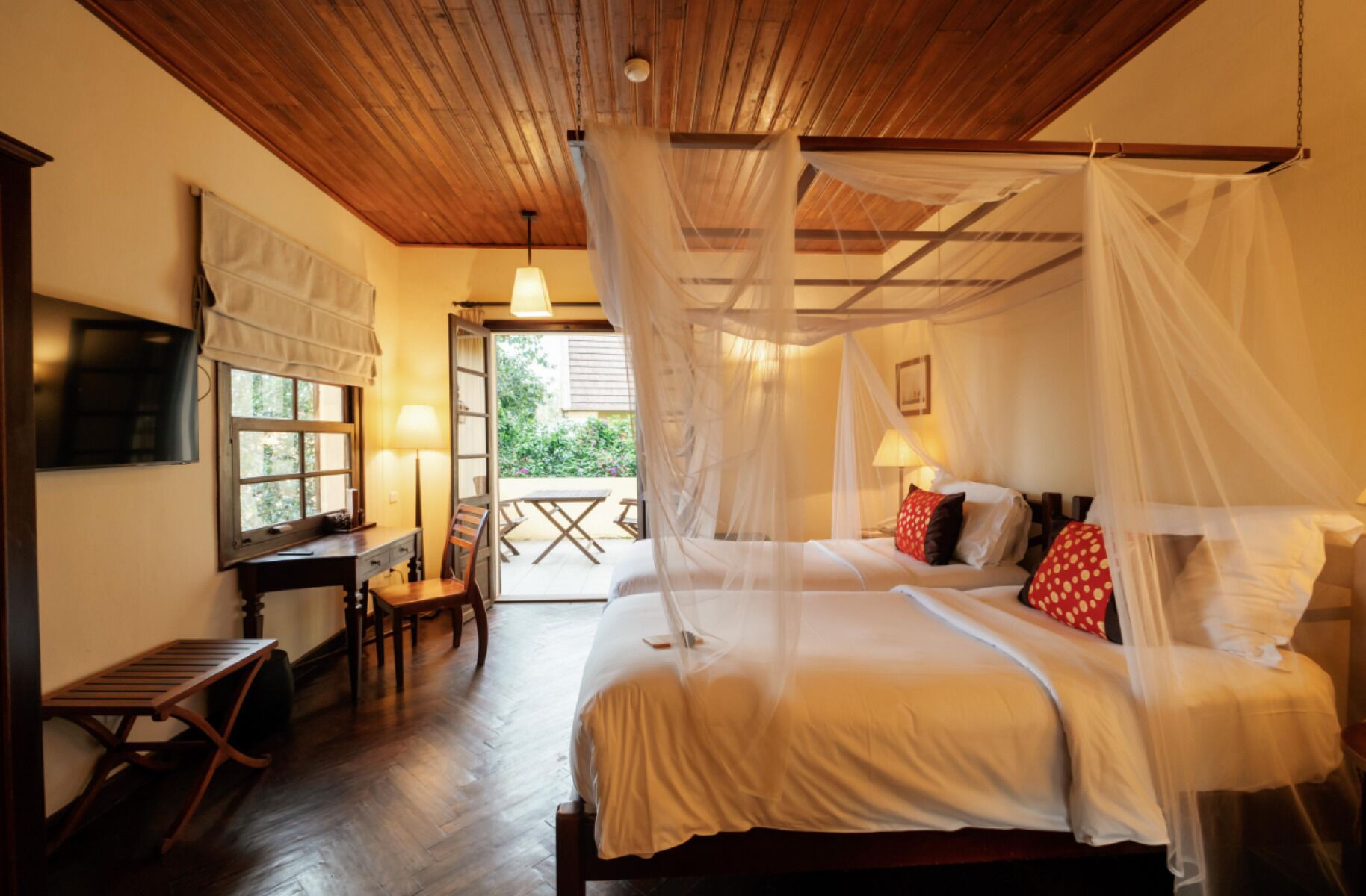 A bedroom with a canopy bed, a desk with a chair, and a view of the outdoors.