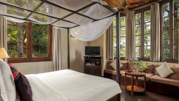 A bedroom with a bed, a TV, a sofa, and large windows.