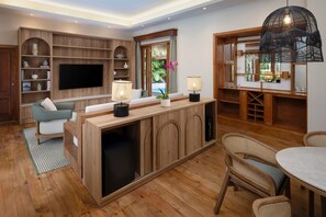 A modern living room with a wooden entertainment unit, a flat-screen TV, a dining area with wicker chairs, and a large window with curtains.