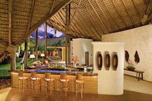 A bar area with wooden chairs and a counter, surrounded by a thatched roof structure. - Zoetry Agua Punta Cana - All Inclusive (Punta Cana)