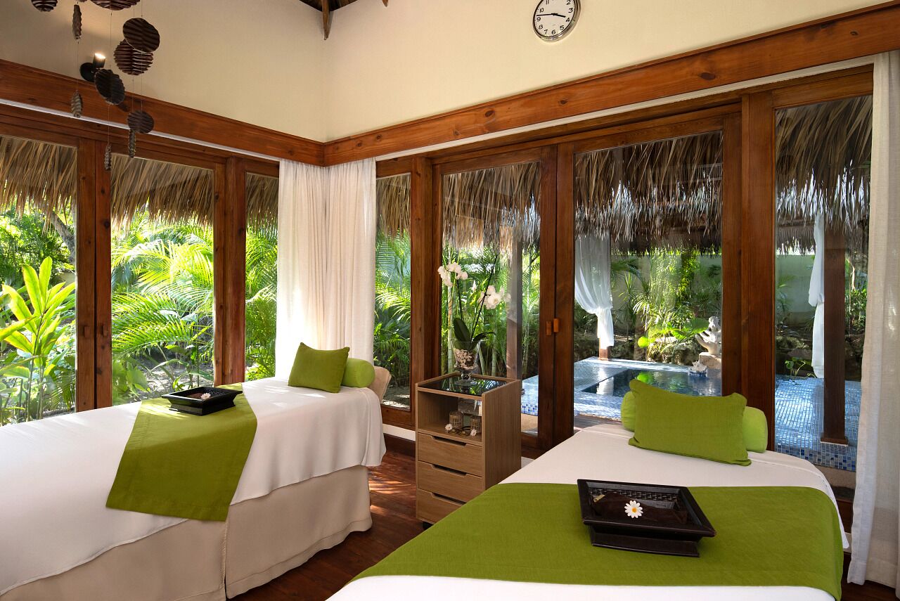 Quarto com duas camas, teto de madeira, relógio e vista para uma piscina.