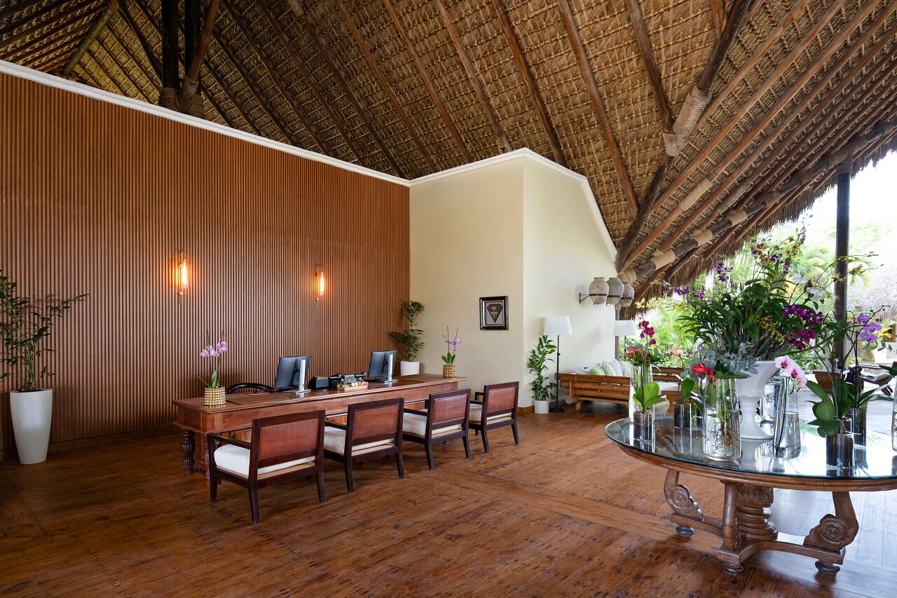 A dining area with a wooden table and chairs, a glass-top table, and potted plants.