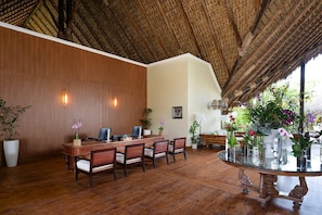 A dining area with a wooden table and chairs, a glass-top table, and potted plants.