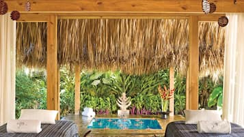A room with two beds, a pool, and a view of lush greenery.