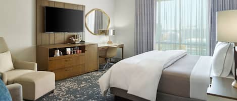 A hotel room with a bed, a desk, a chair, a TV, and a large window with curtains.