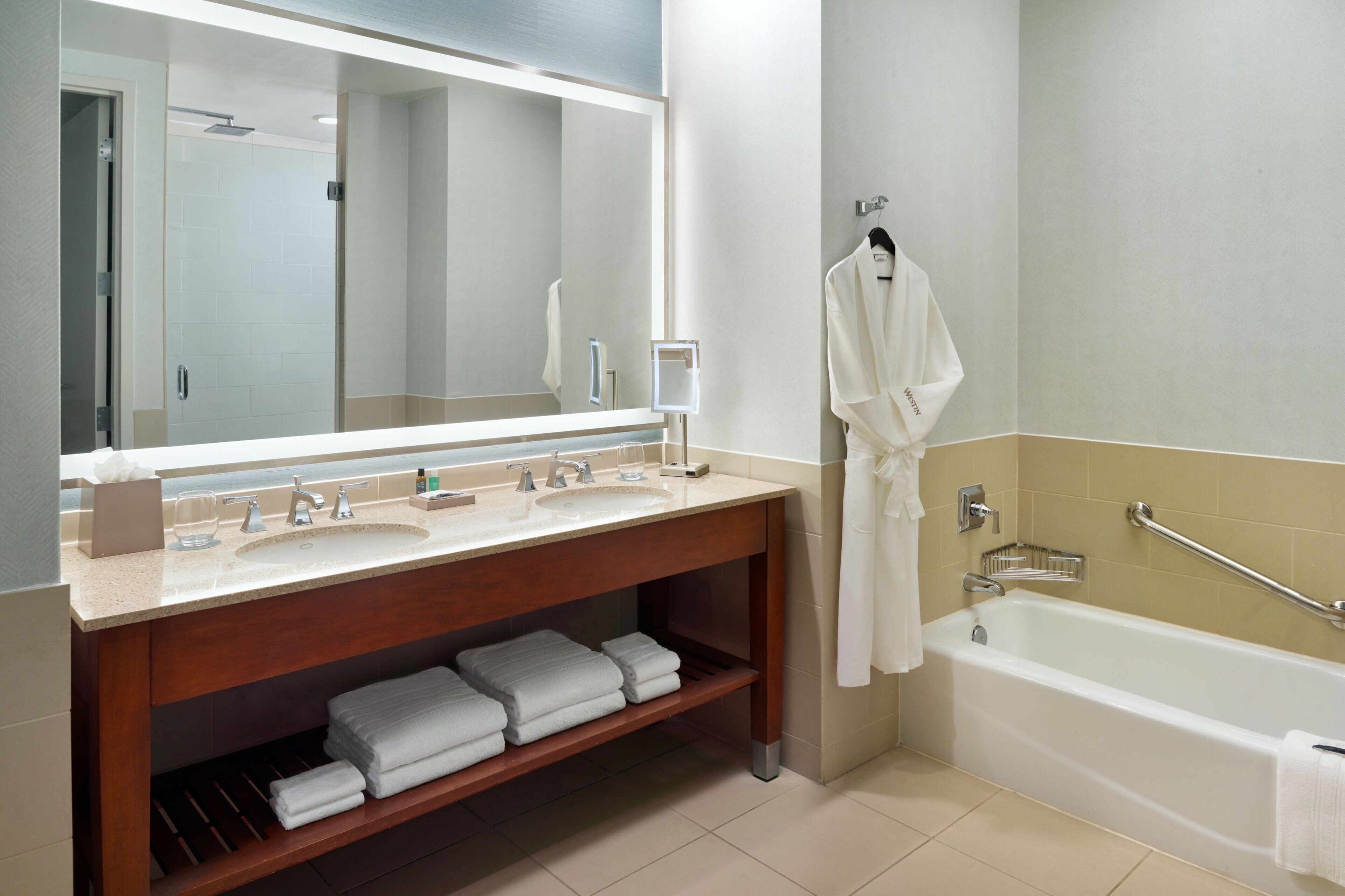 A modern bathroom with a large mirror, a sink, a bathtub, and a towel rack.
