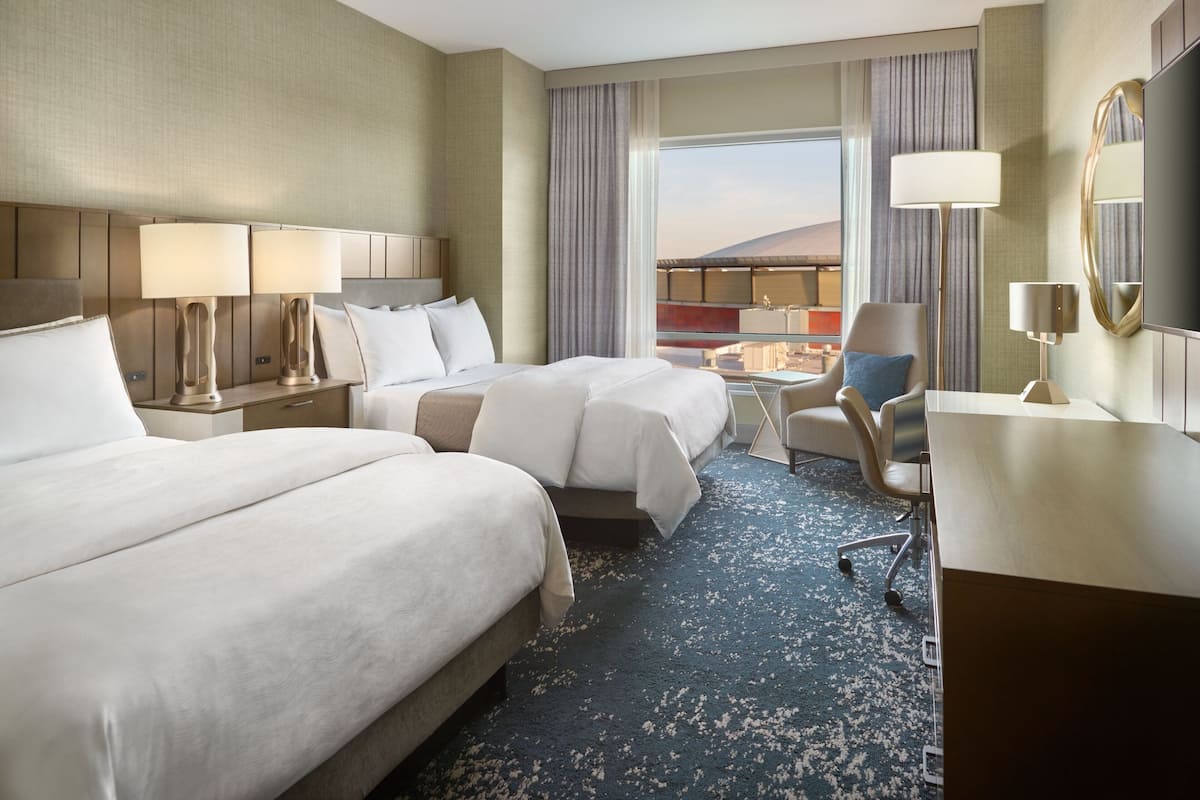 A hotel room with two beds, a desk, a chair, and a large window with a view.