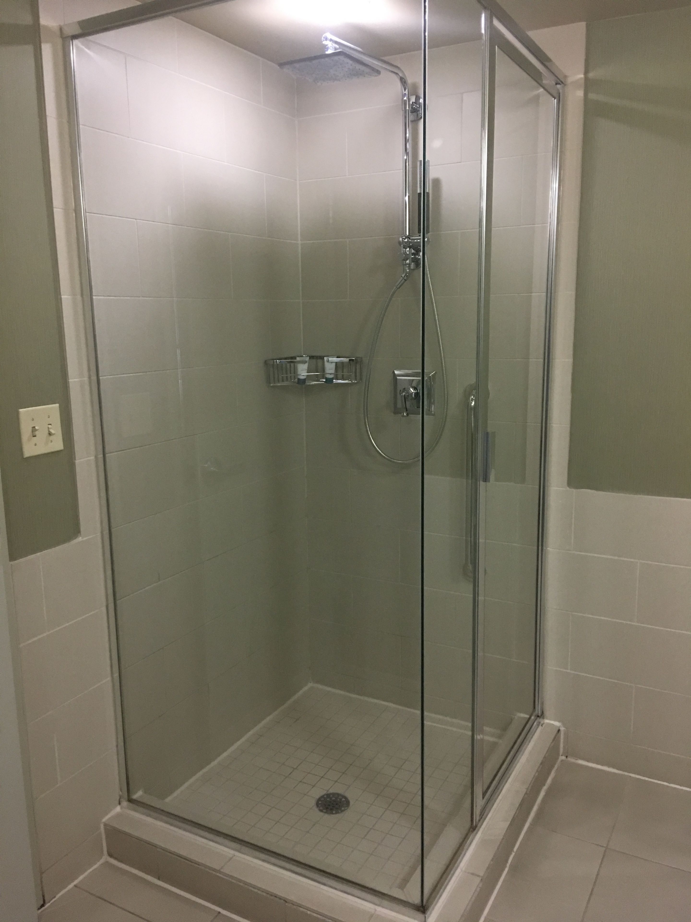 Eine Duschkabine mit Glaswänden, einer Handbrause und einem am Wand montierten Wasserhahn.