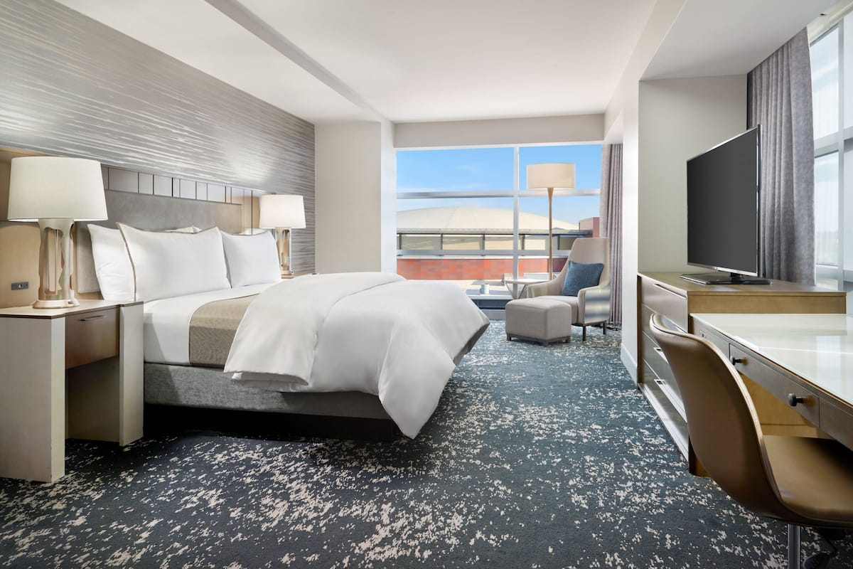 A hotel room with a bed, desk, chair, TV, and a view of the beach.