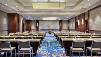 A conference room with rows of tables and chairs, a podium, and a large screen at the front.