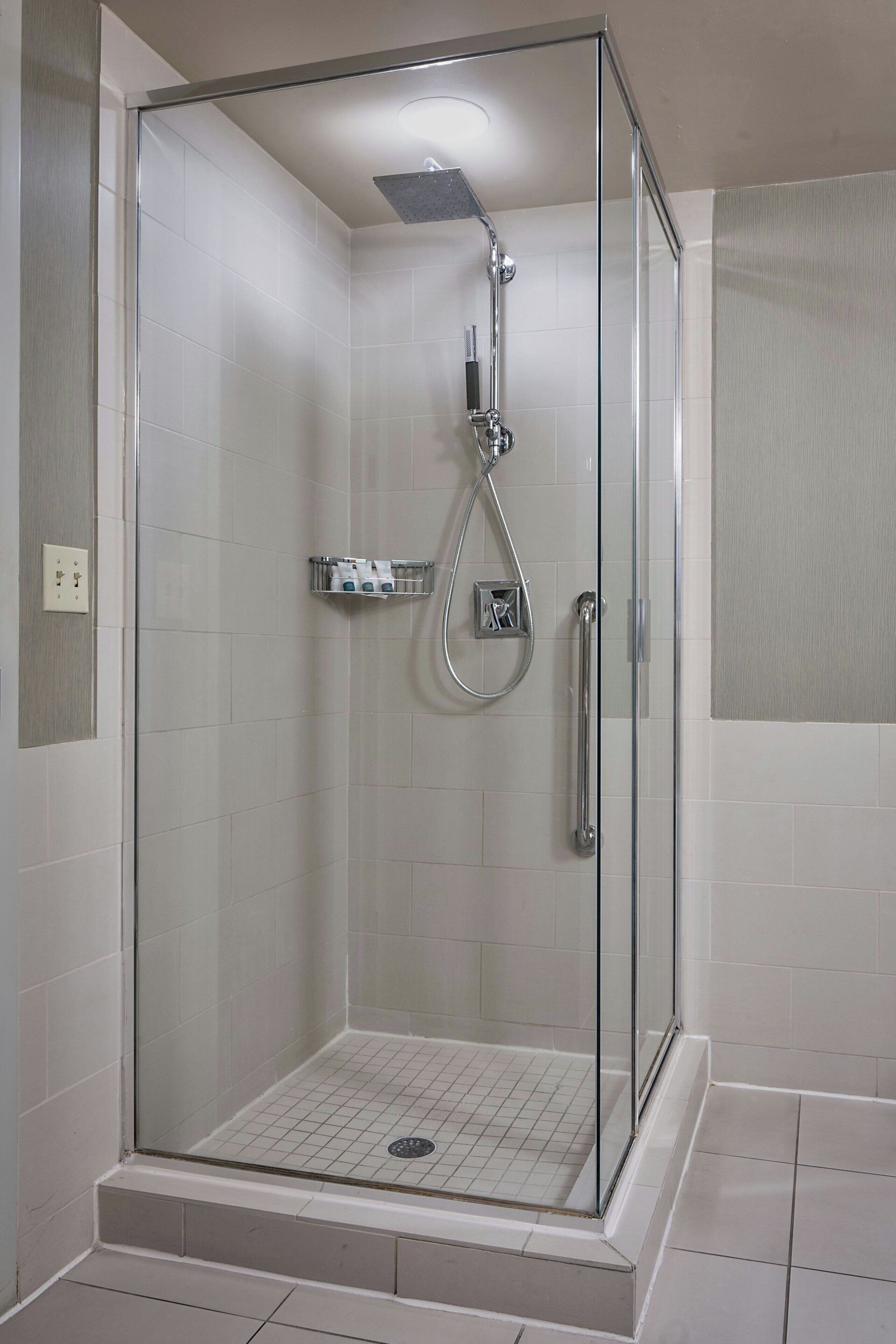 Een douche met glazen wand, een handdouche en een kraan op de muur.