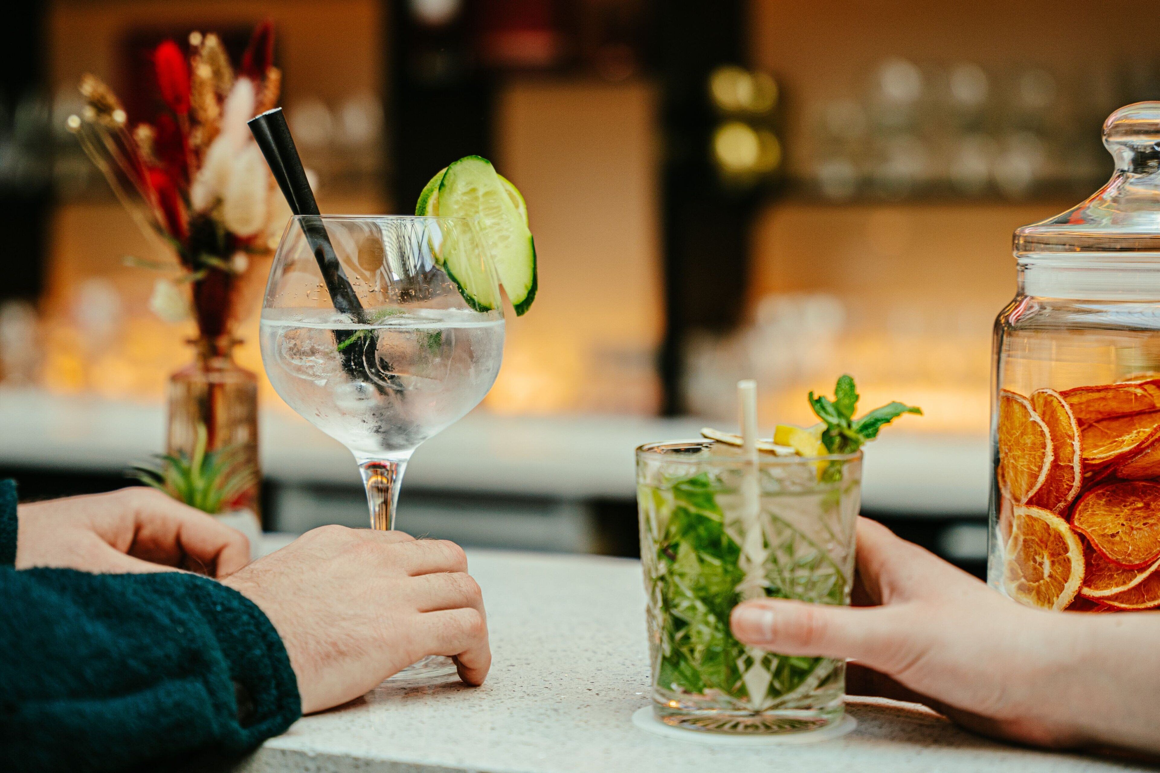 A bar setting with a glass of water, a glass with mint and cucumber, and a jar of dried fruit.