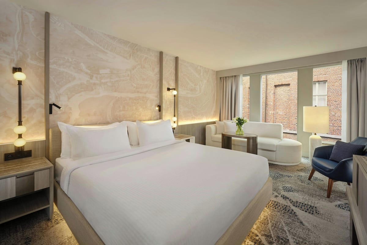 Habitación de hotel con una cama grande, un escritorio, una silla y vistas a un edificio de ladrillo.