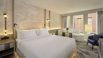 Habitación de hotel con una cama grande, un escritorio, una silla y vistas a un edificio de ladrillo.