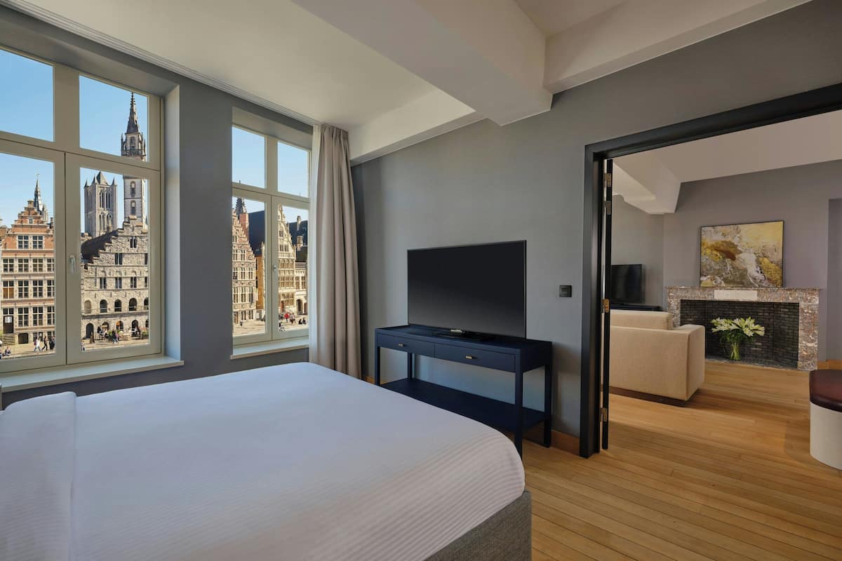 Habitación de hotel con una cama grande, televisión, chimenea y vistas a edificios históricos.
