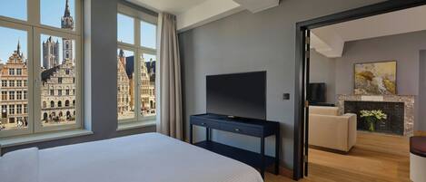 A hotel room with a large bed, a TV, a fireplace, and a view of historic buildings.