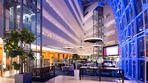 Un moderno vestíbulo de hotel con techo alto, paredes de vidrio y varias zonas de comedor.
