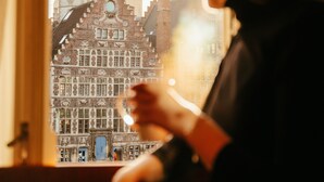 Una persona sentada junto a una ventana con vista a un edificio histórico con una torre de reloj.