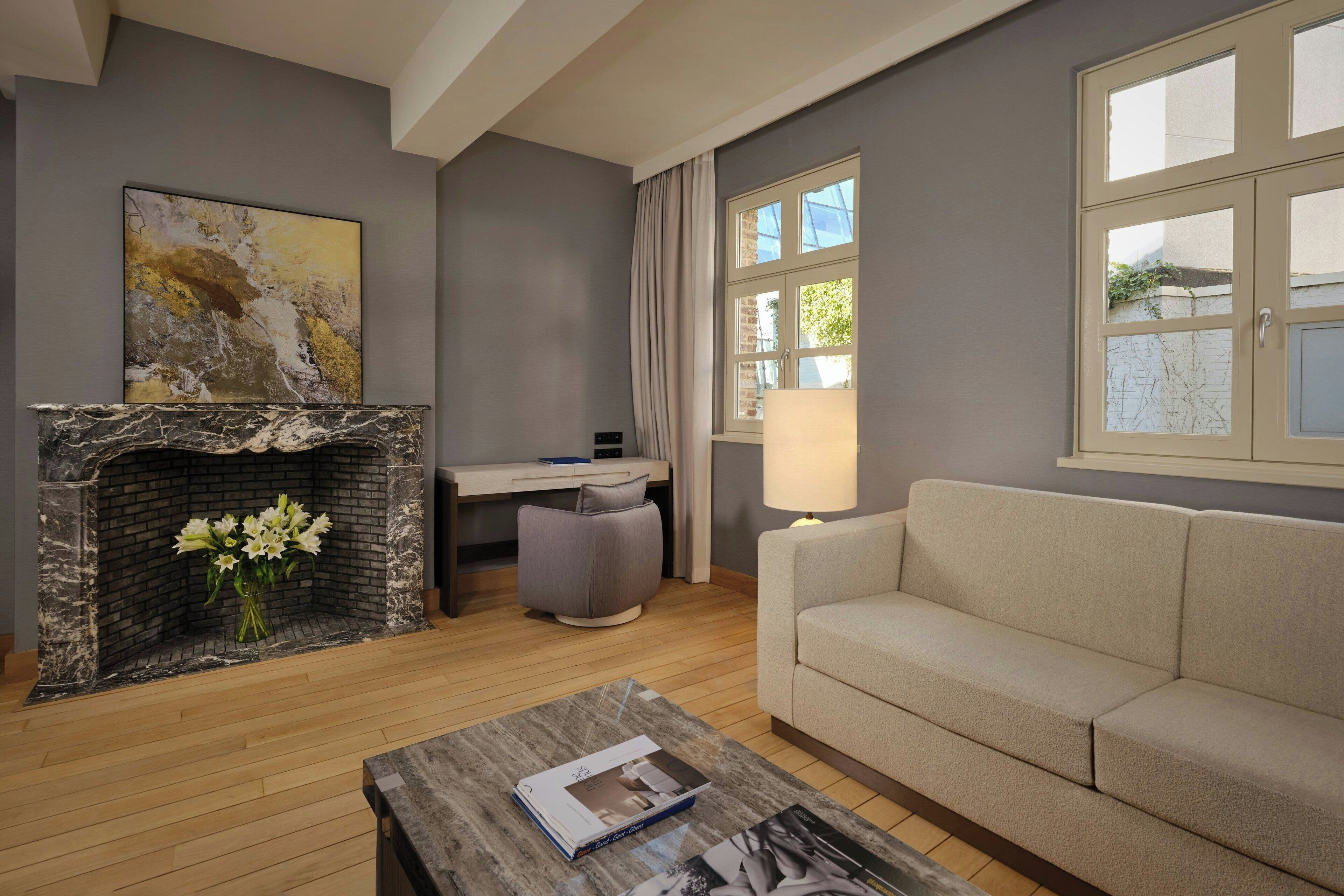 A living room with a fireplace, a sofa, a coffee table, a desk, and a window with curtains.