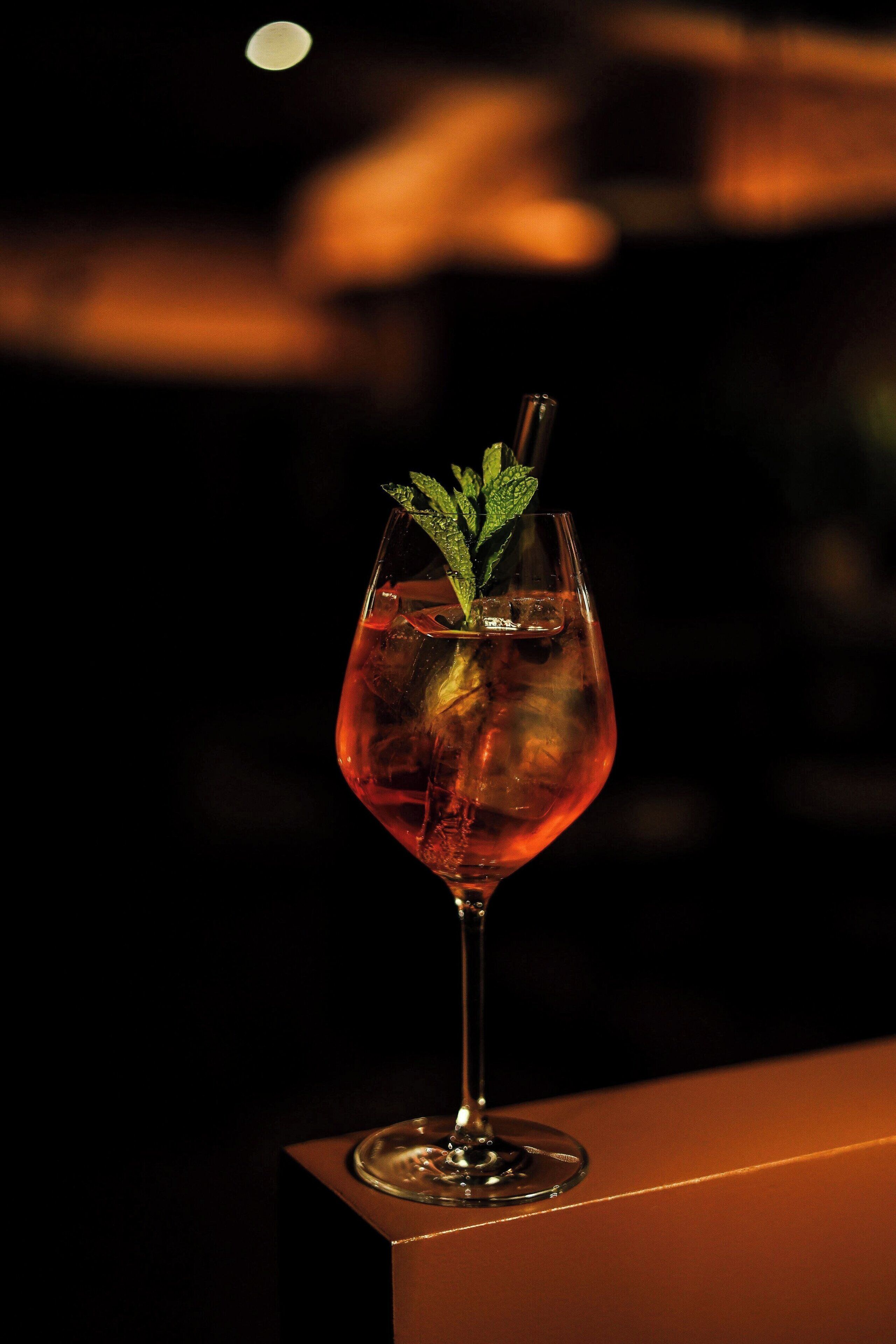 A glass of red drink with mint garnish on a table.